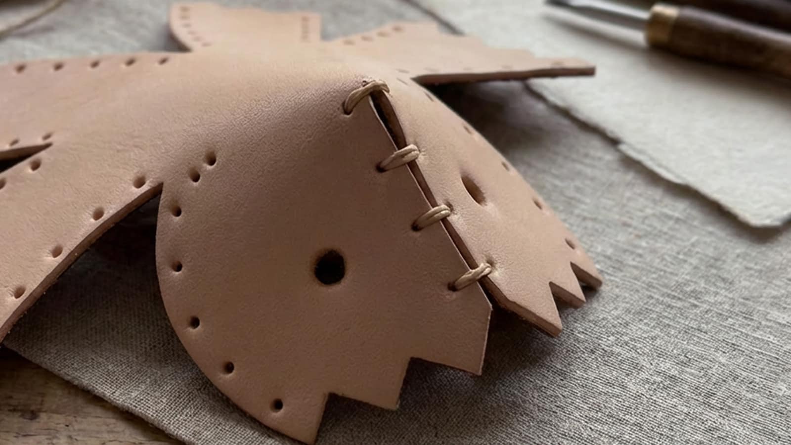 Hand-stitched leather parts beginning to rise from a flat surface, forming the first curve of a leather model.
