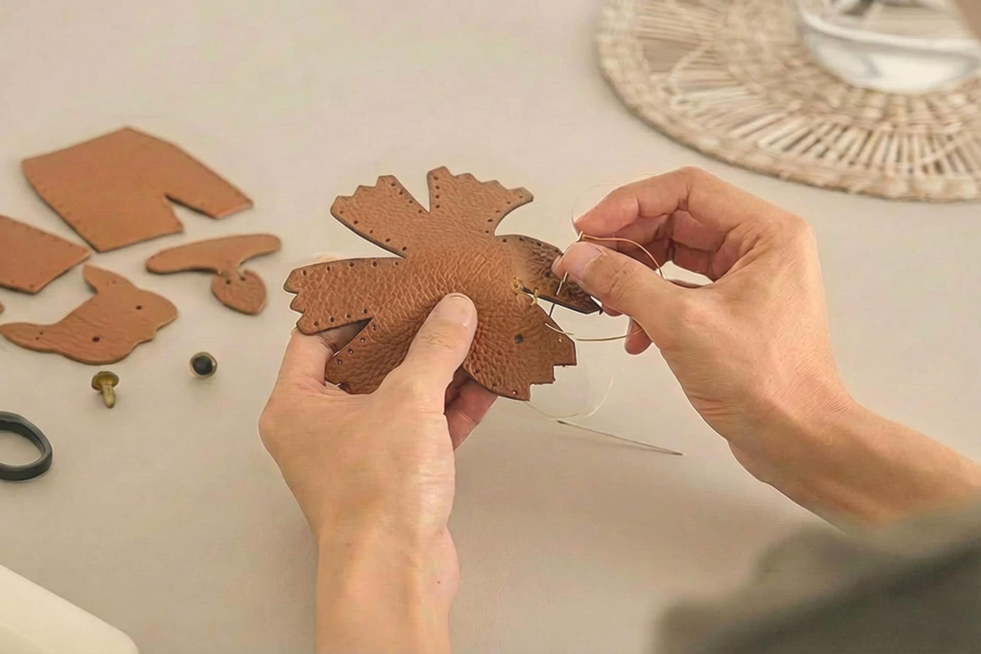 Hands stitching pieces of brown leather for a Leather DIY Kit on a quiet worktable.